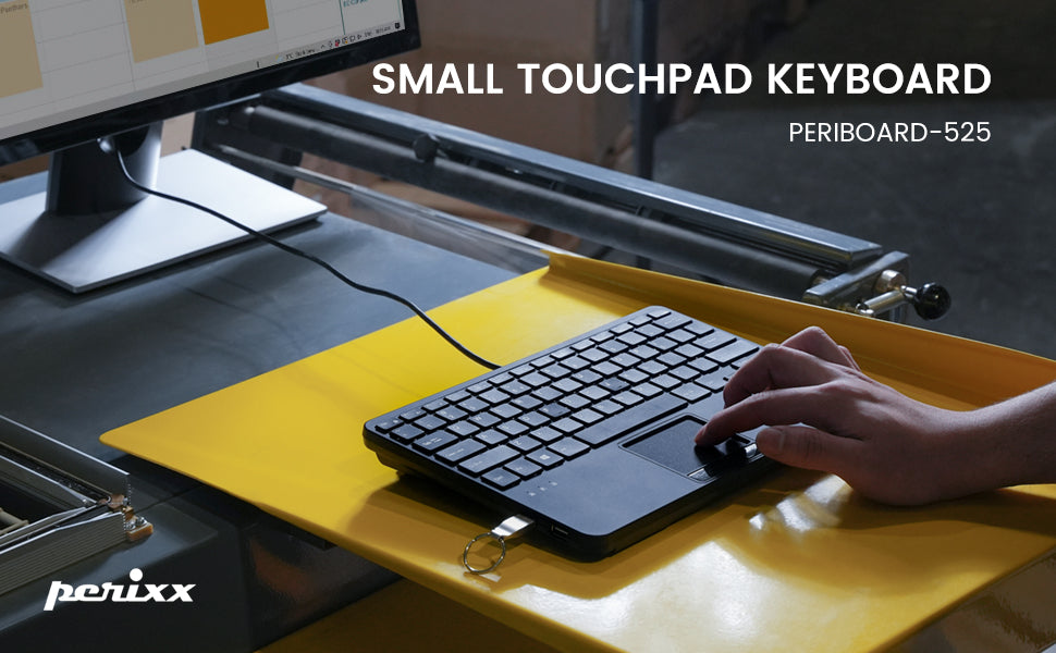 Small touchpad keyboard on yellow desk surface. Compact design with integrated touchpad. Model Periboard-525 by Perixx. Hand shown using the device.