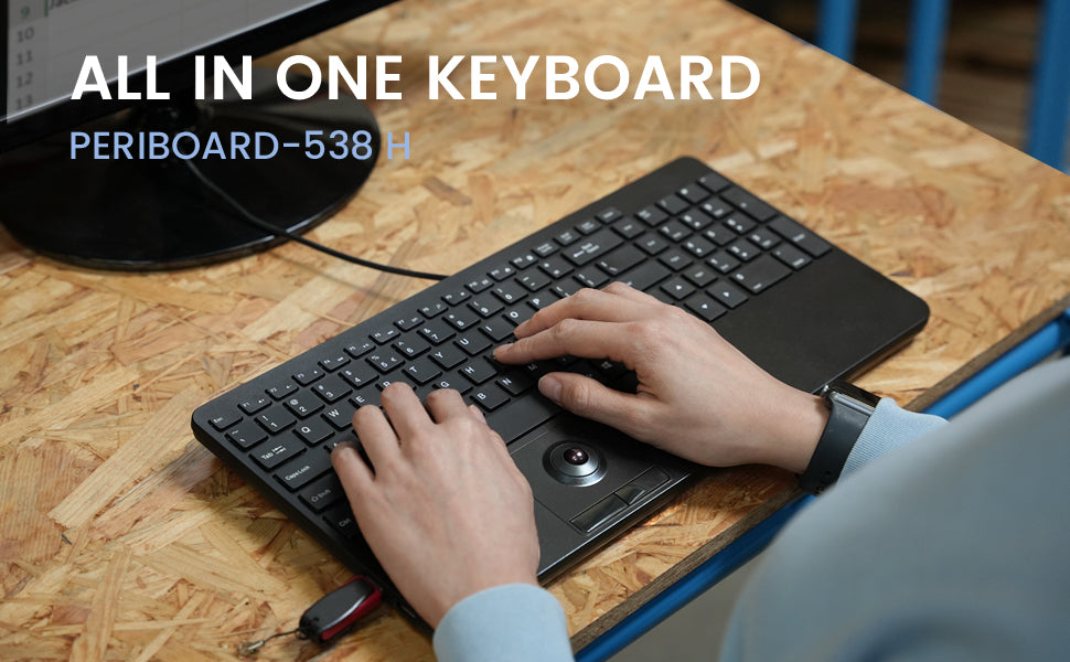 All-in-one keyboard labeled Periboard-538 featuring full-size layout with integrated trackpad, shown in use on wooden surface.